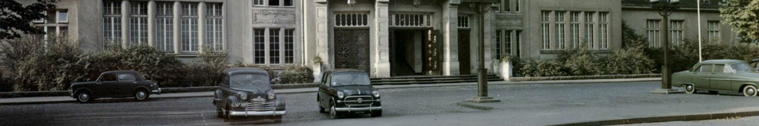Drei Oldtimer parken vor einem großen Gebäude mit hohen Fenstern und einem reich verzierten Eingang.