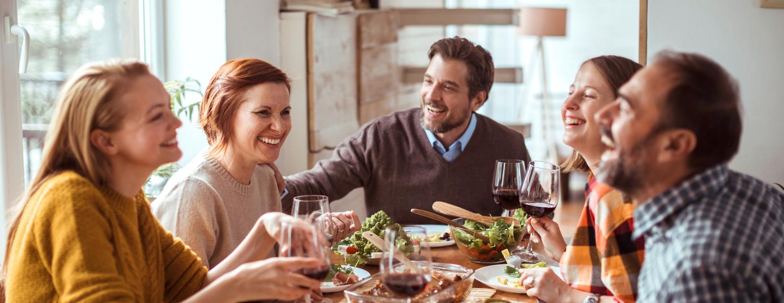 Personengruppe an einem Tisch, prosten mit sich mit Wein zu, essen & lachen