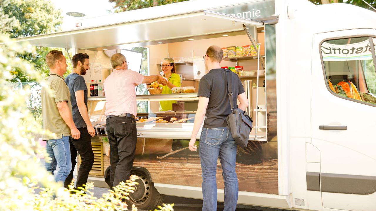 People standing in line at a food truck, ordering from a person inside.