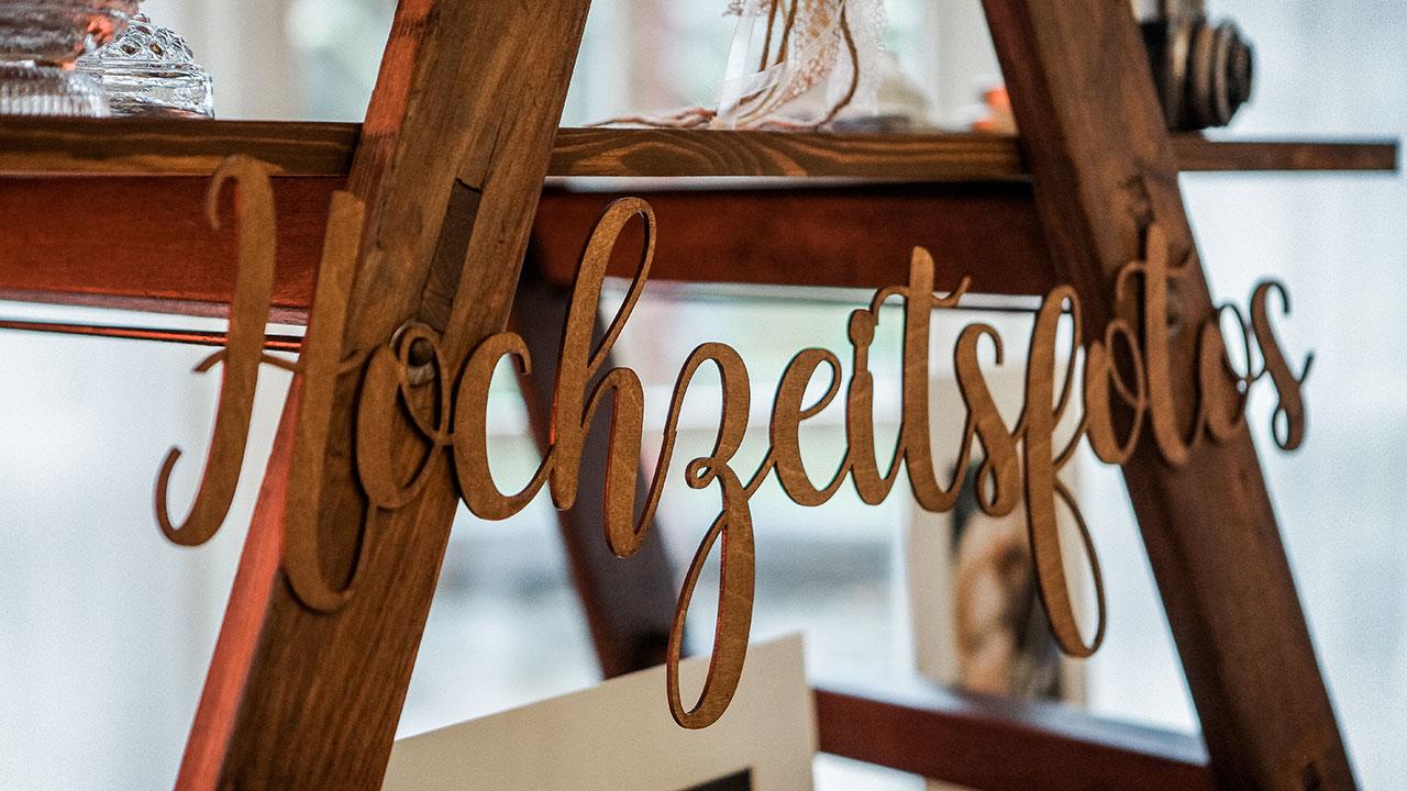 Wooden sign with the word "Hochzeitsfotos" hanging from a wooden structure at a wedding display.