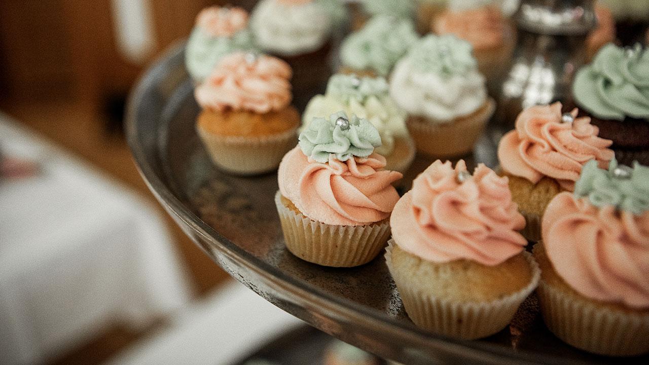 A tray of cupcakes with pastel-colored frosting swirls and decorative silver beads.