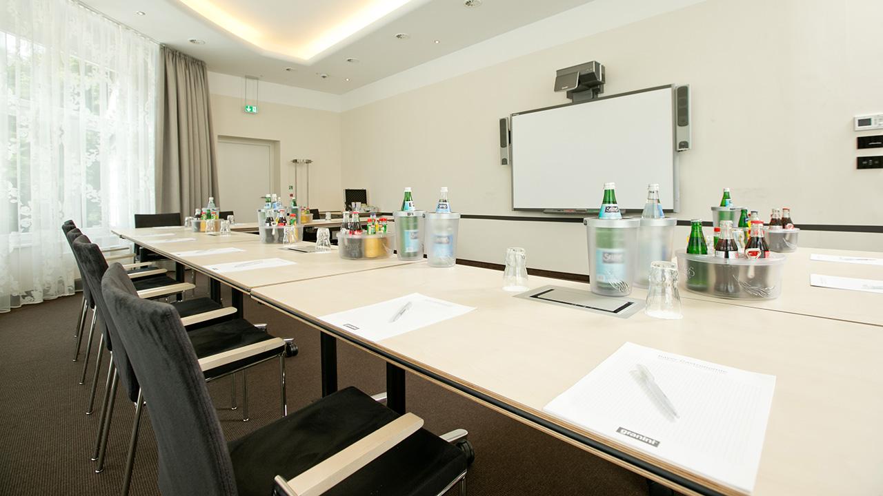 A conference room with a long table set with notepads, pens, bottled drinks, and ice buckets. There's a whiteboard and projector at the front.