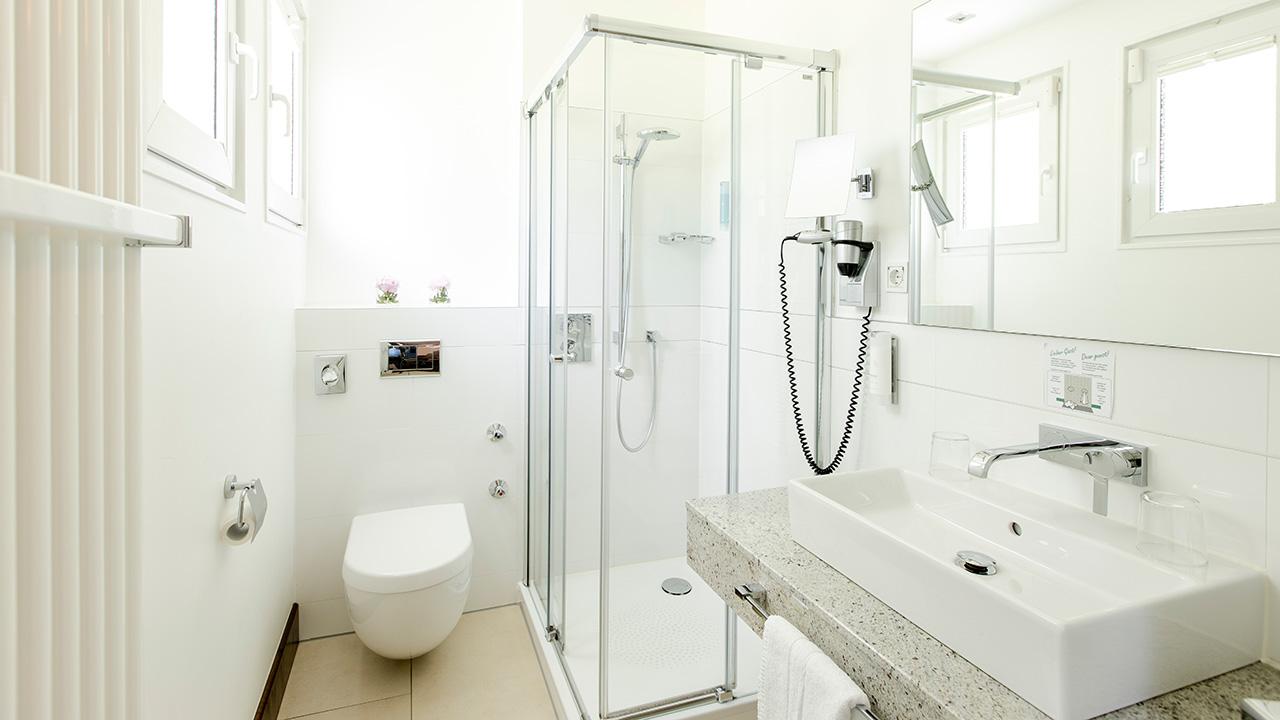 A modern bathroom with a glass shower, white sink, wall-mounted toilet, and a hairdryer on the wall.