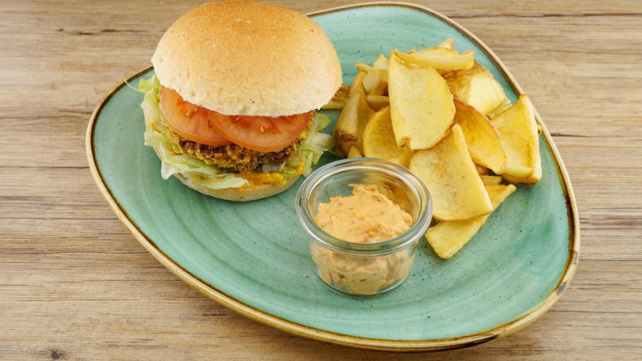 A burger with lettuce and tomato, served on a green plate with potato wedges and a small jar of sauce.