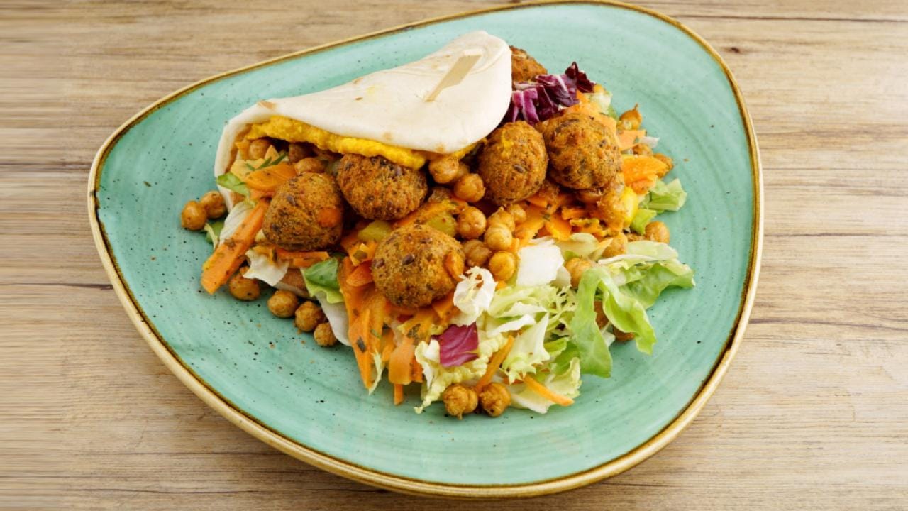 A dish with falafel, chickpeas, shredded carrots, and lettuce is served on a turquoise plate with a piece of flatbread.