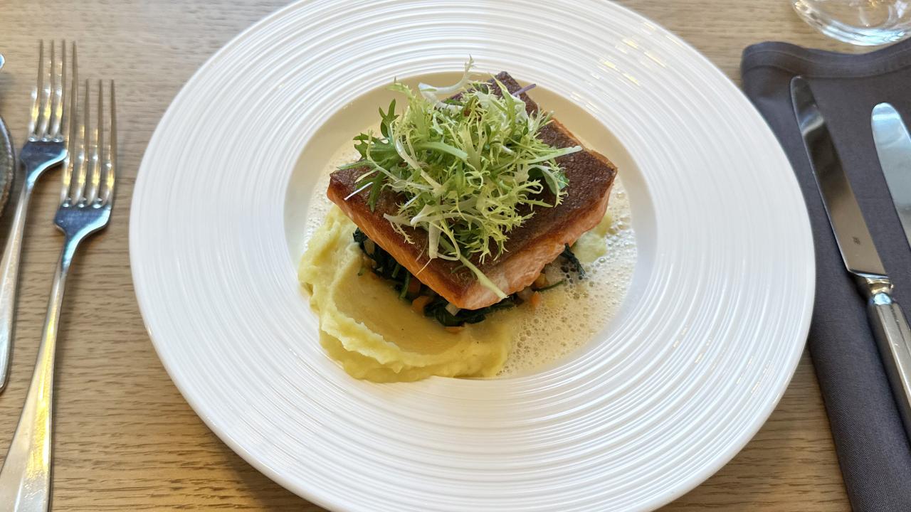 Gedeckter Tisch im Restaurant mit einem Stück Lachsforelle auf Püree und einer hellen Schaumsauce. 
