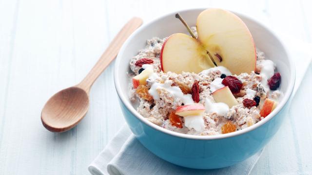 A bowl of muesli topped with apple slices and dried berries, placed beside a wooden spoon on a folded napkin.