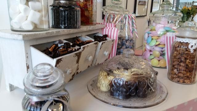 Assorted colorful candies and chocolates displayed in glass jars on a shelf, with a decorative glass dome covering some of the sweets.