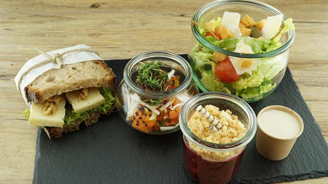 Schwarzes Schiefertablett mit einer belegten Stulle, einem Salat im Weckgas und zwei kleinen Desserts in Gläschen.