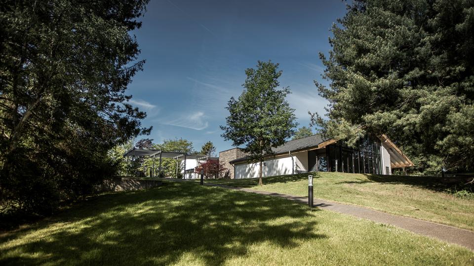 A modern building surrounded by trees and a grassy lawn under a clear blue sky.